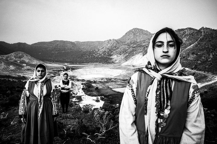A man and two women wearing the costumes of Nisyros, stand by the volcano