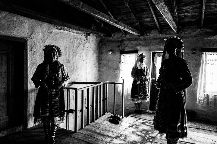 Three women wearing the local costumes of Mani in Evros, standing inside an old local house.