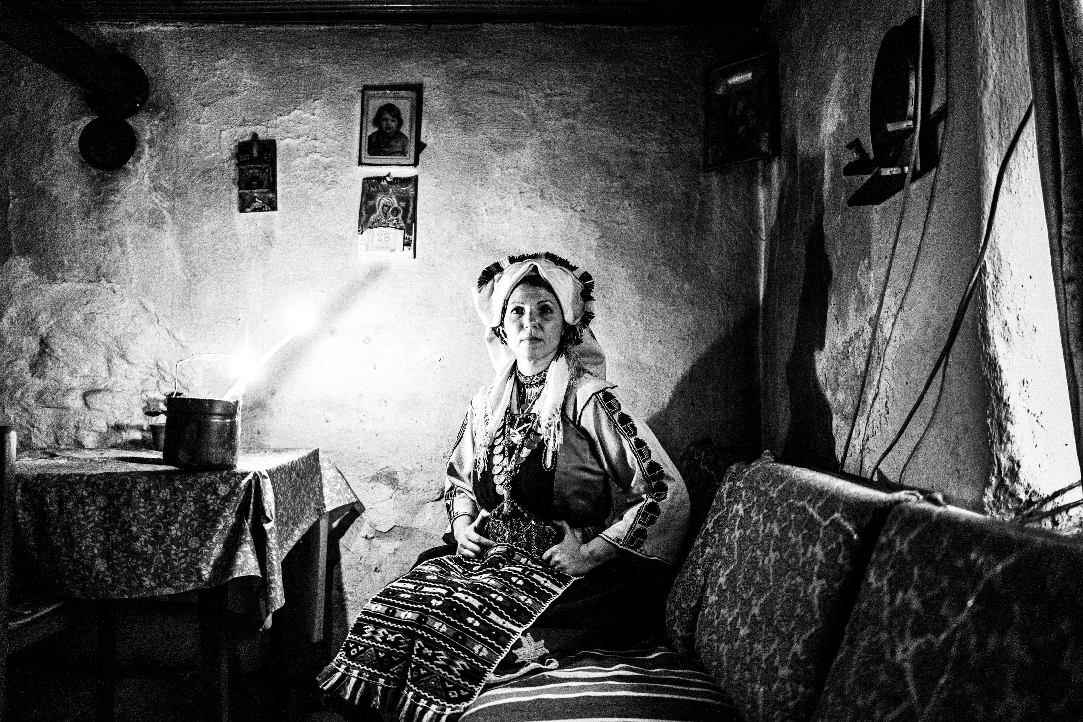 Woman wearing the local costume of Mani, Evros, sitting on a sofa in candlelight inside a local house