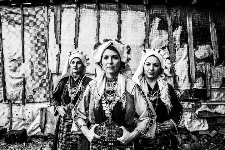 Three women wearing the local costumes of Mani in Evros, standing outside an old local house.