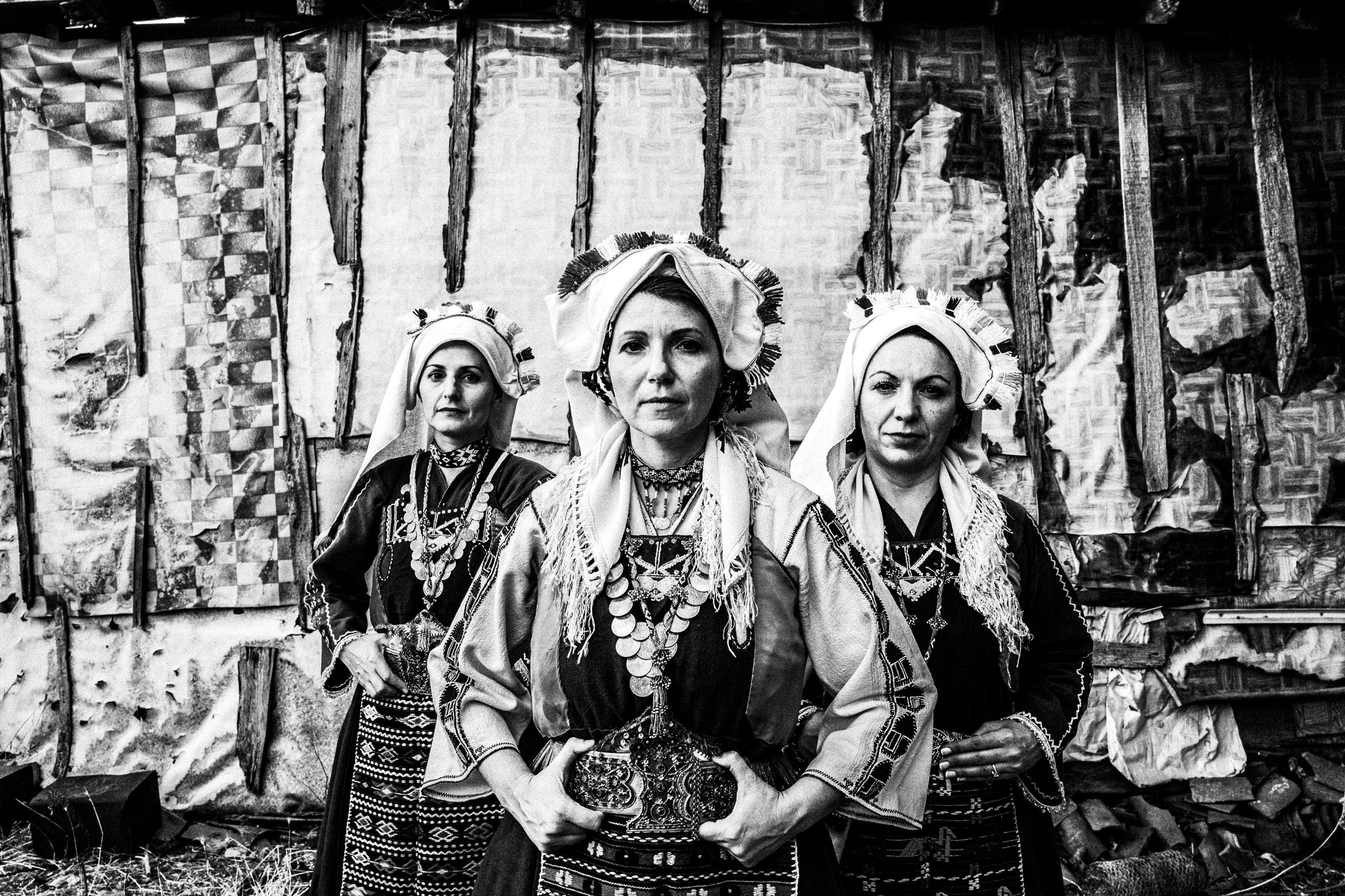 Three women wearing the local costumes of Mani in Evros, standing outside an old local house.