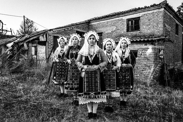 Women wearing the local costumes of Mani, Evros, posing in formation outside a local house.