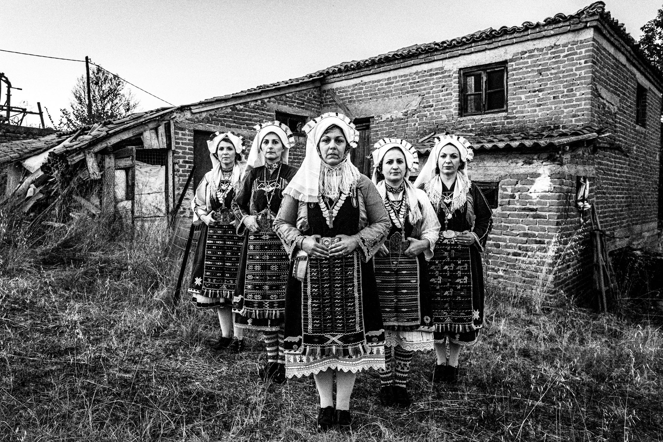 Women wearing the local costumes of Mani, Evros, posing in formation outside a local house.