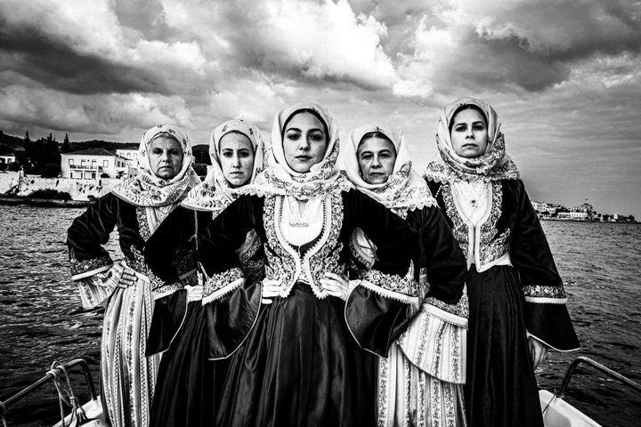 Five women in formation on a boat, wearing the local urban dresses of Spetses at sea overlooking the Kapetaneika houses