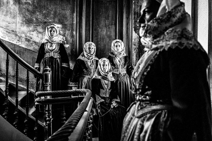 Women wearing the local costumes of Spetses, standing around a wooden staircase inside Anargyros mansion on the island of Spetses
