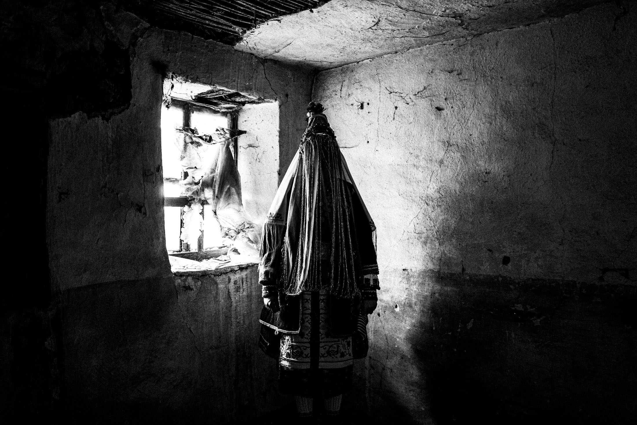 A veiled bride in the traditional dress of Orini Serron, Macedonia, standing by a window in a local house