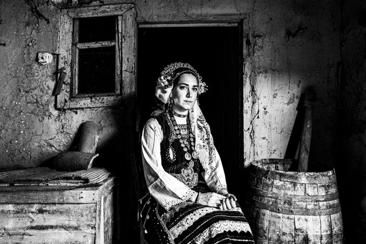 A woman wearing the local costume of Metaxades, sitting by the door inside an old local house.