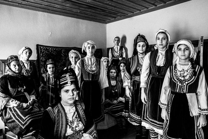 A large group of young women wearing the local costumes of Prosotsani in Drama, inside a local house