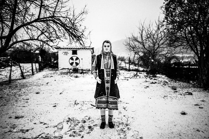 A woman wearing the local costume of Volax in Drama, standing in the snow in the village.