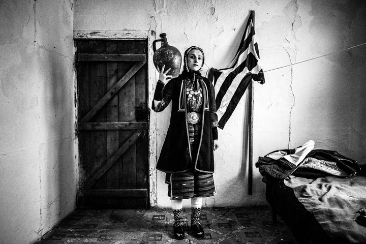 A woman wearing the local costume of Volax in Drama, standing inside a local home.
