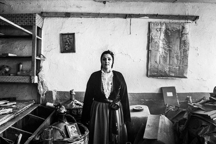 A woman wearing the urban dress of Pelion, standing inside an old local shop near Portaria.