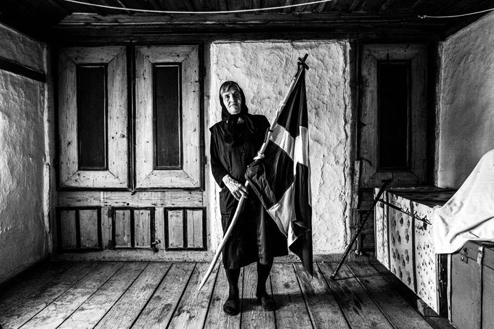 An elderly woman holding a greek flag inside her home at Metaxades