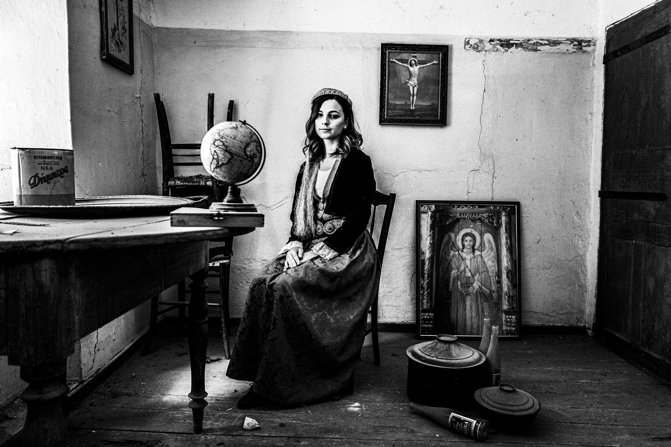 A woman wearing the urban dress of Pelion, sitting inside an old local house in Pinakates