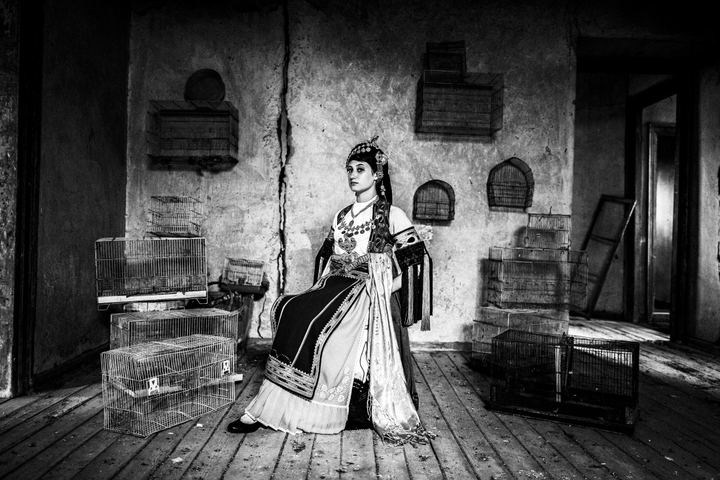 A woman wearing the traditional Karagouna dress, sitting inside an old local mansion among bird cages