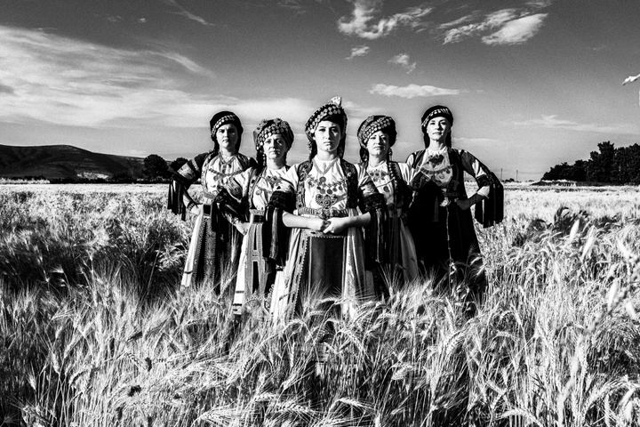 Five women in the traditional Karagouna costumes standing in formation in a local wheat field near Trikala
