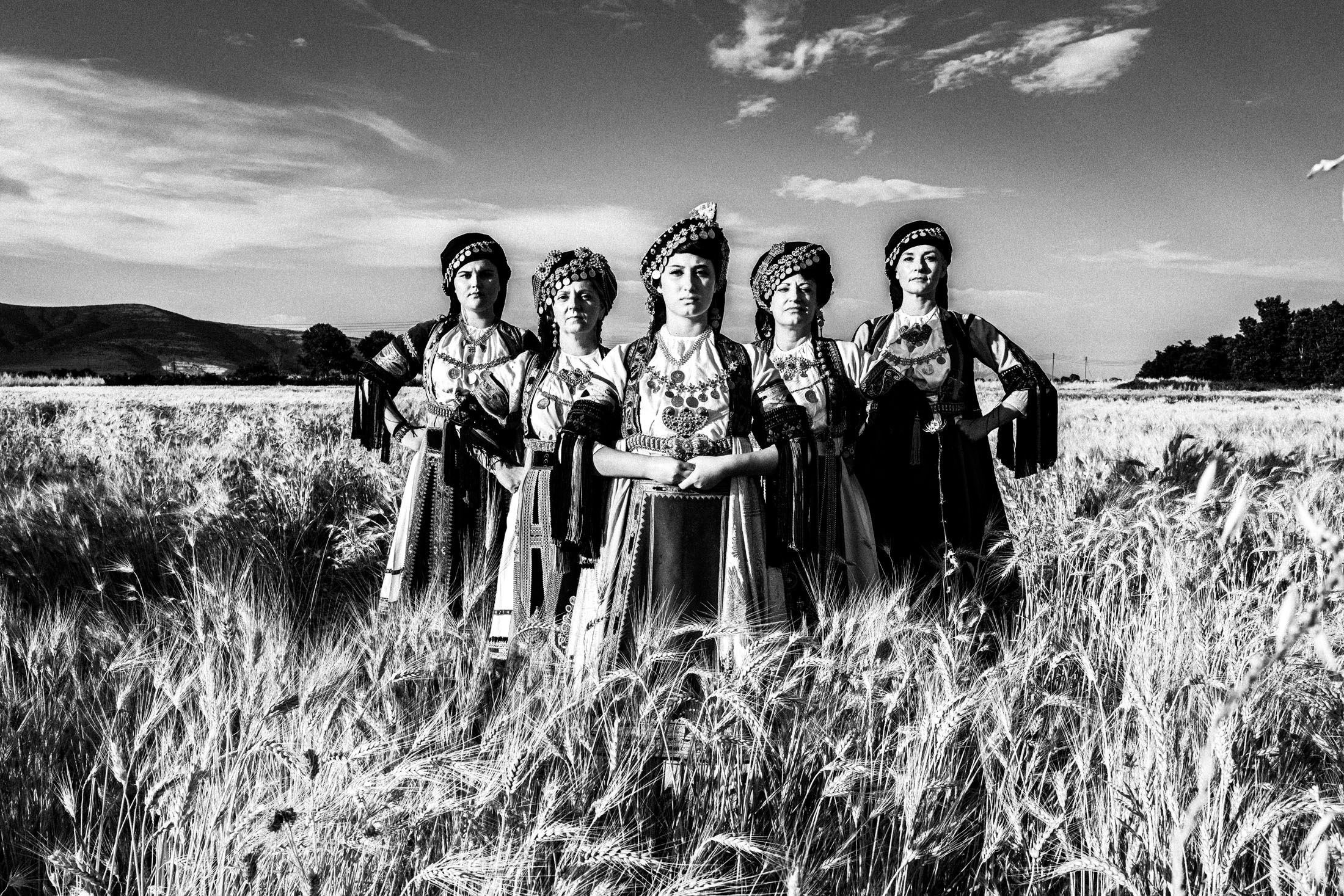 Five women in the traditional Karagouna costumes standing in formation in a local wheat field near Trikala