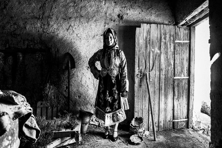A woman wearing the costume of Stefanovikio in Thessaly, standing by a wooden door in a local barn