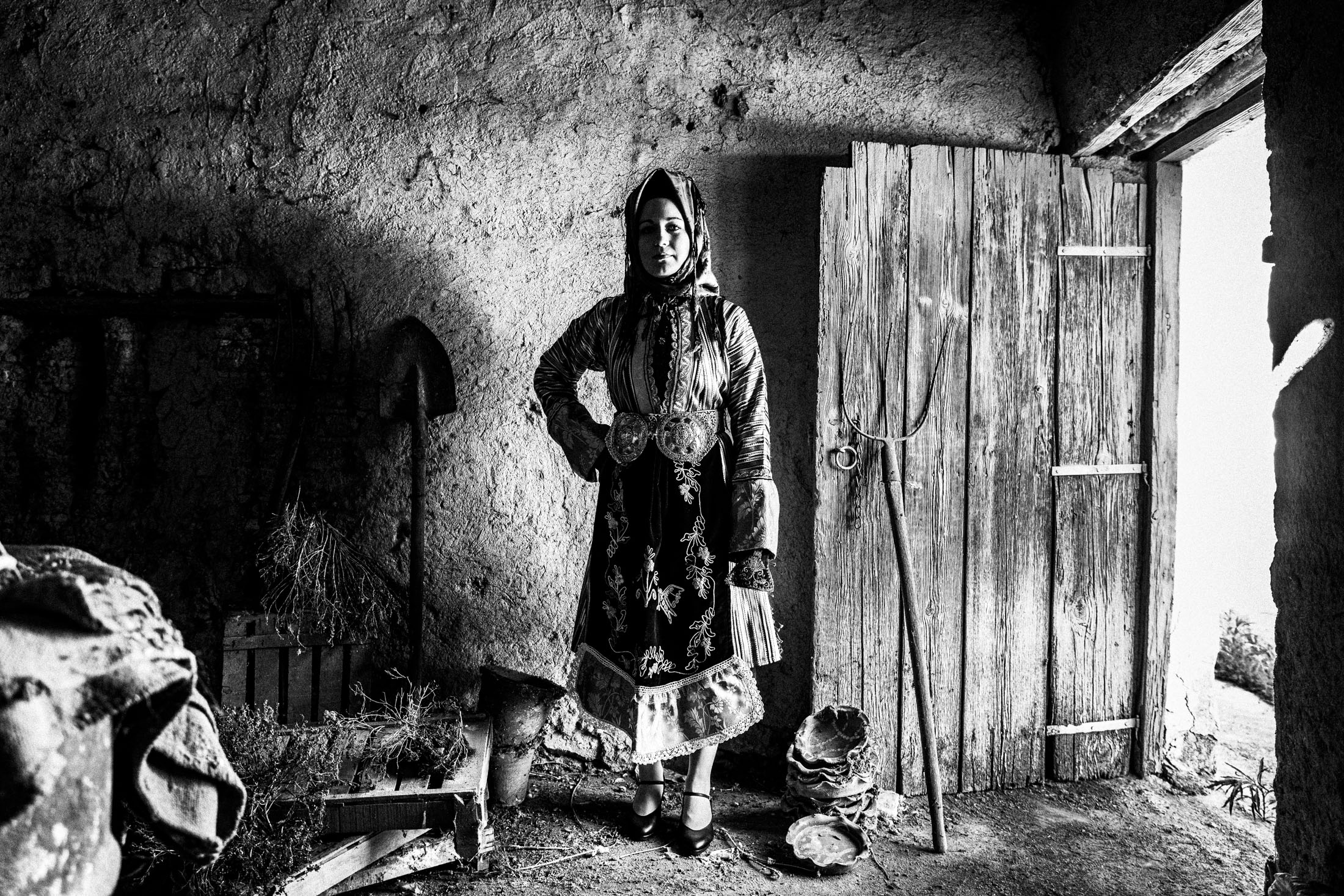 A woman wearing the costume of Stefanovikio in Thessaly, standing by a wooden door in a local barn