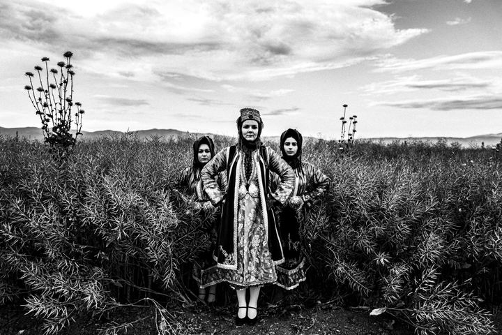 Three women wearing the local costumes of Stefanovikio, standing in a local field of canola.
