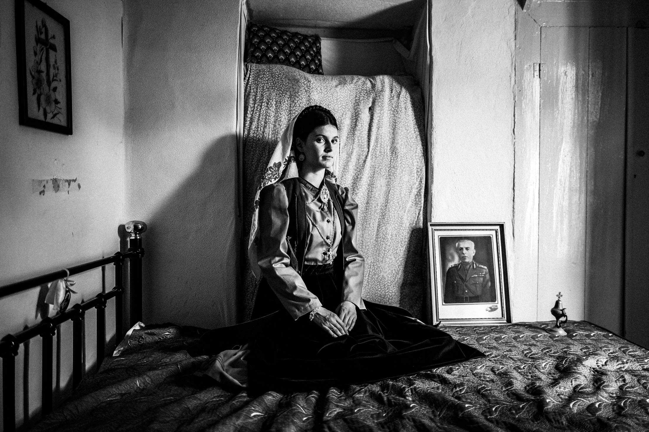 A woman wearing the local dress of Platanos, Nafpaktia, inside a local house sitting on a bed