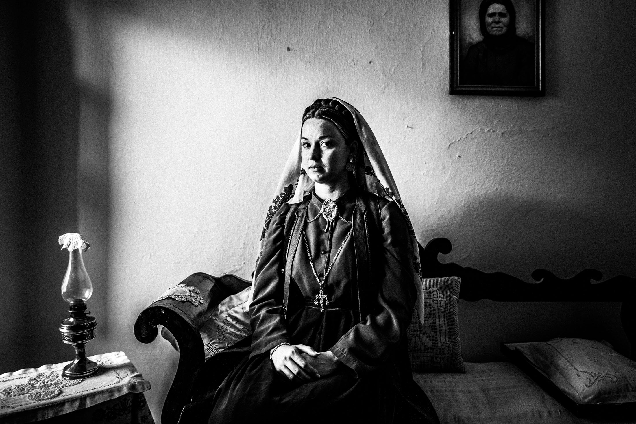 A woman wearing the local costume of Platanos in Nafpaktia, sitting by a window inside a local house