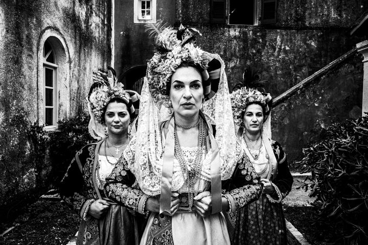 Three women in the costumes of Central Corfu posing in formation in a traditional local settlement