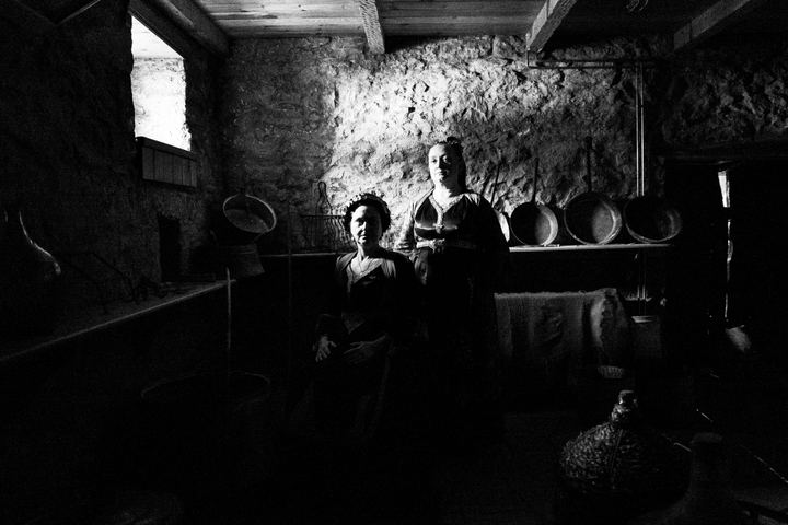Two women wearing the local dresses of Metsovo in Epirus, inside a dark local warehouse.