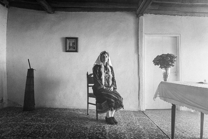 A seated women wearing the costume of the Arvanites group of the southern villages of Evros, sitting on a chair inside a local house in Mani, Evros, Thrace