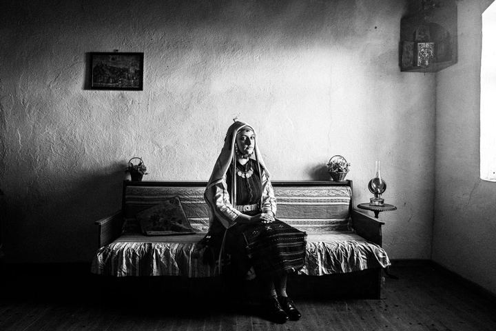 A young woman in the local dress of Ormenio, Evros, seated on a sofa inside a local house in Mani, Thrace