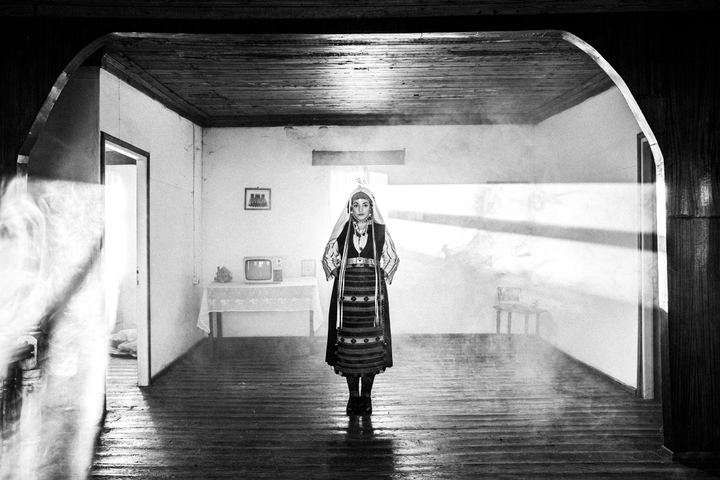A young woman wearing the local dress of Ormenio, inside a backlit old local house.