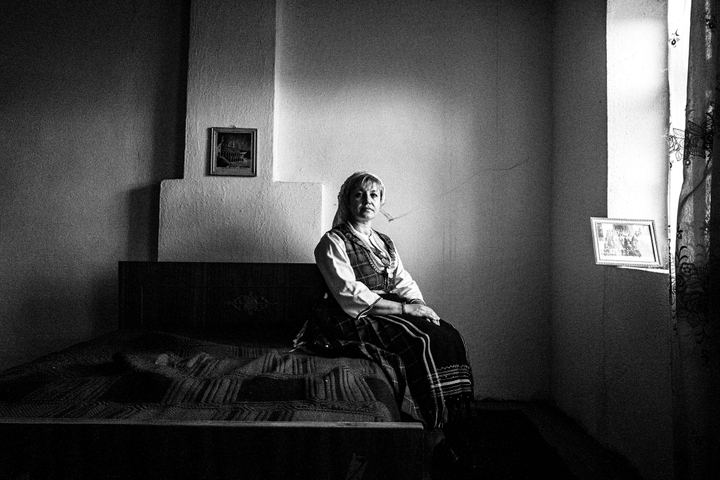 A woman wearing the costume of Eastern Romylia, seated on a bed by a window inside a local house in Mani, Evros, Thrace