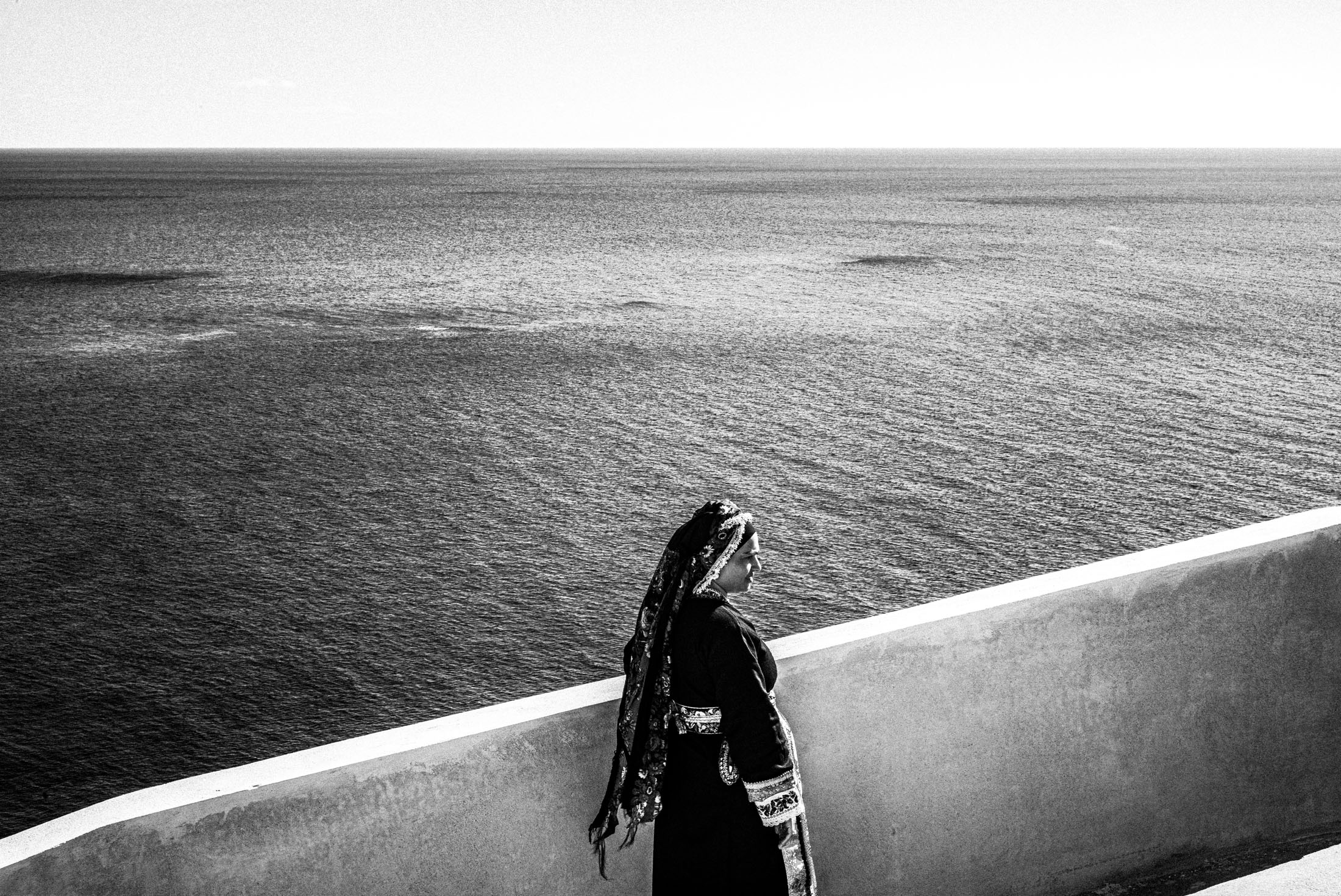 A woman dressed in the local traditional costume of Olympos, Karpathos against the sea going up a white staircase.