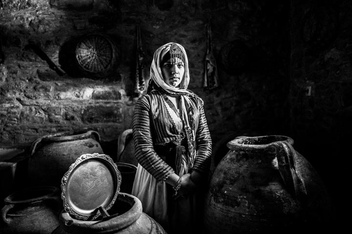 A woman wearing the local costume of Gennadi in Rhodes, standing among urns at a local stone warehouse