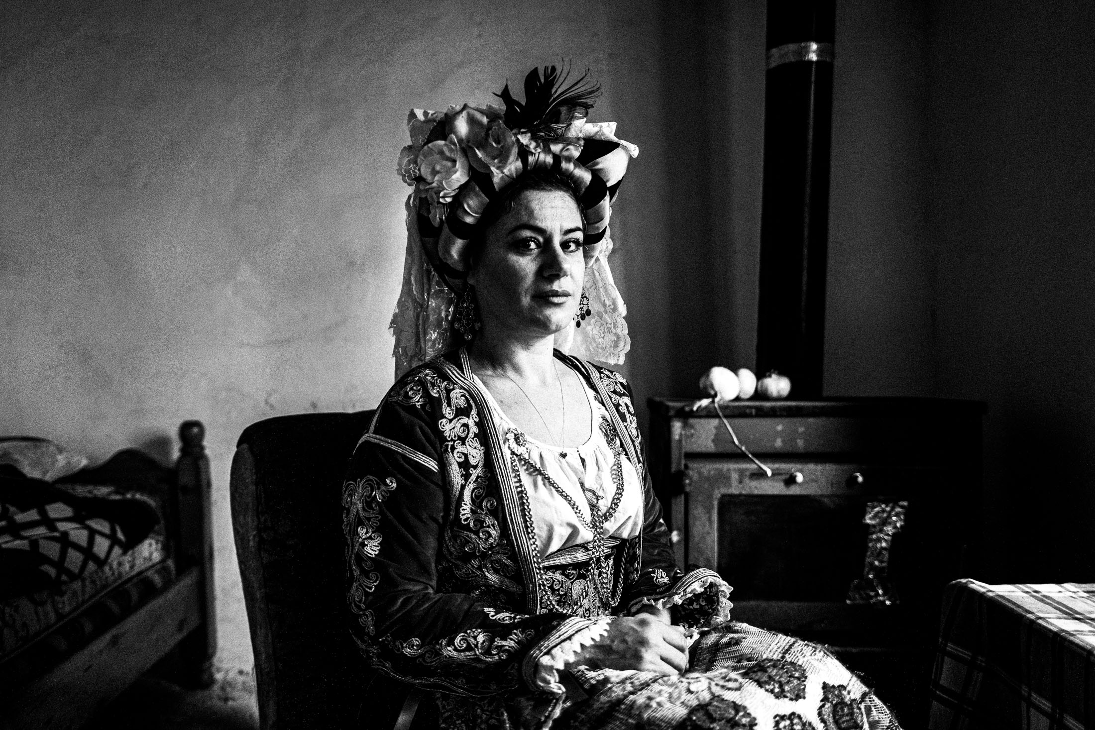 A woman wearing the local costume of Southern Corfu, sitting in an armchair by a stove inside a local old house in Korakades village