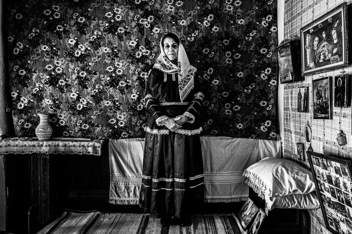 A woman wearing the costume of Afantou, Rhodes, against a floral wallpaper inside a local house