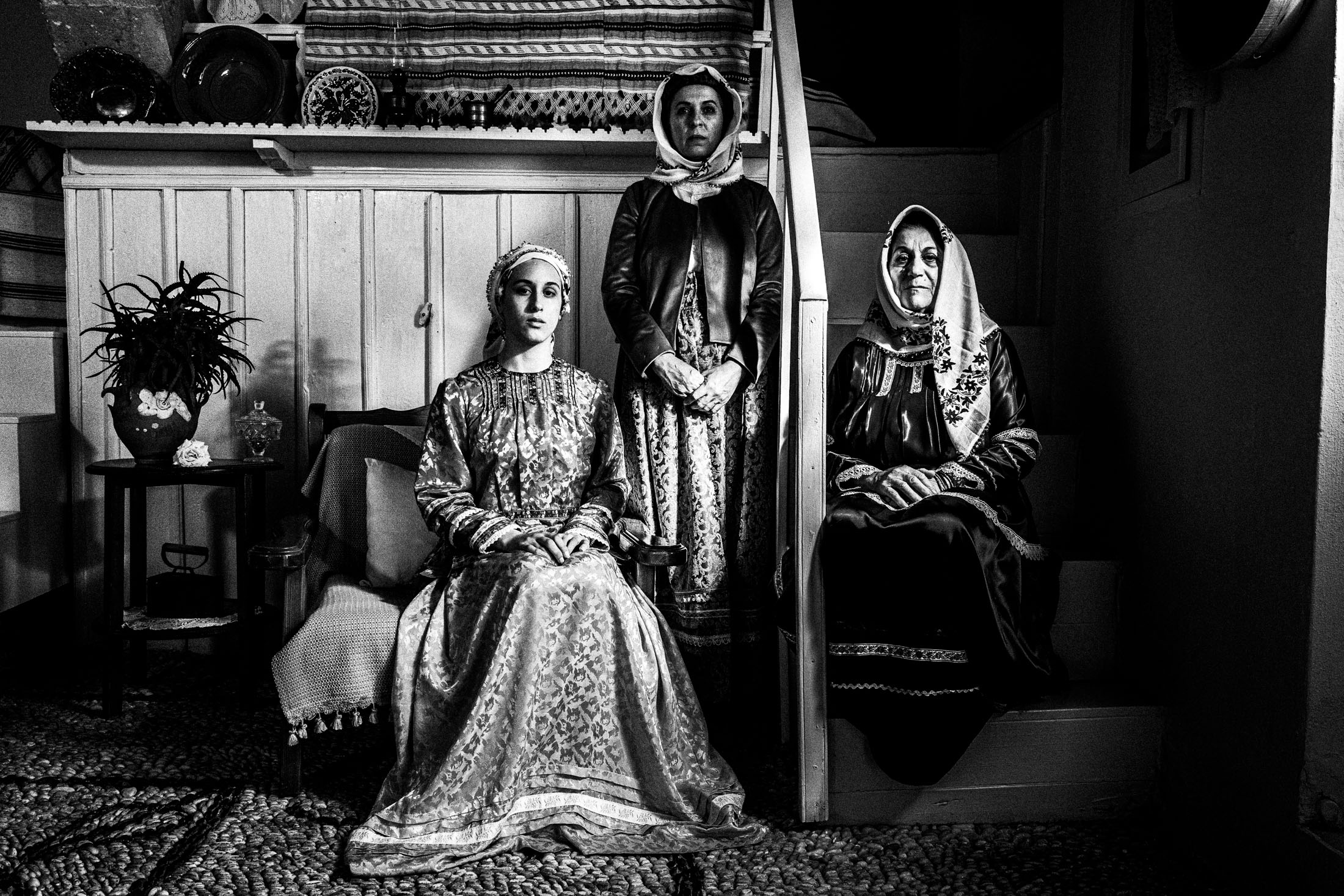 Three women wearing the costumes of Afantou, Rhodes, posing by a staircase inside a local house.