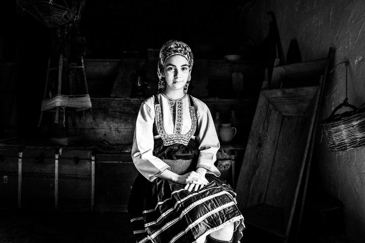 A young woman wearing the local costume of Emponas in Rhodes, sitting by the door inside a local traditional house, serving as the folklore museum