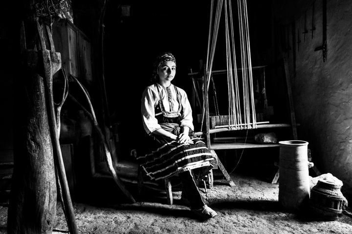 A young woman wearing the local dress of Emponas, Rhodes, sitting by a loom inside the local folklore museum