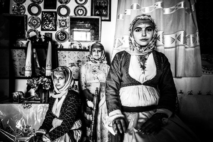 Three young women wearing the local costumes of Apollona in Rhodes, posing inside a local traditional home