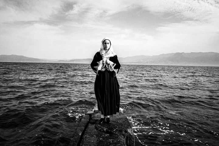 Woman wearing the costume of Kymi, Euboea, standing on a dock by the sea