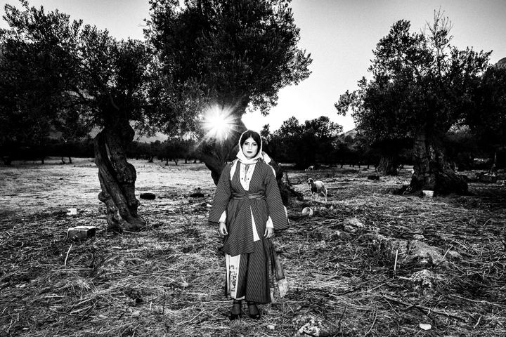 A woman dressed in the traditional costume of Kalymnos, stading in a field among olive trees.