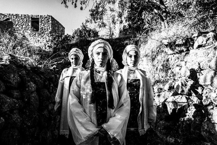 Three women in formation, wearing the local dresses of Vessa in Chios, standing in the sun