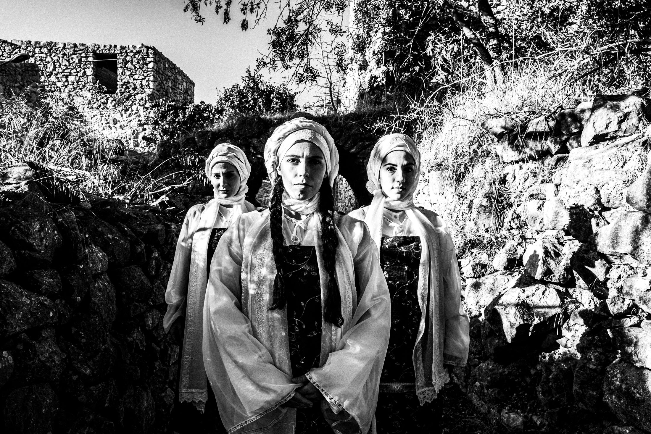 Three women in formation, wearing the local dresses of Vessa in Chios, standing in the sun