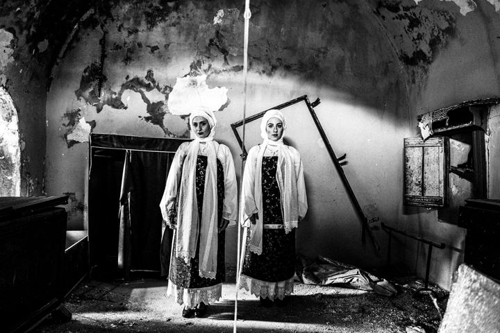 Women wearing the local costumes of Vessa, standing inside a ruined local house