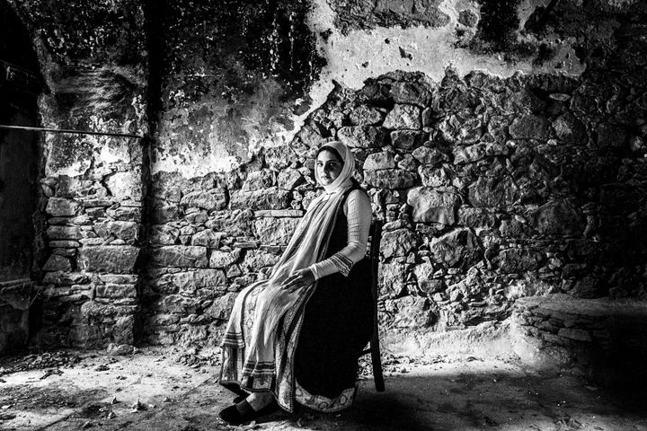 A young woman wearing the local costume of Elata, sitting inside an old stone building