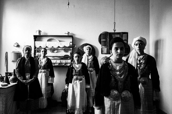Six women wearing the local costumes of Tegea standing inside the kitchen of a local house