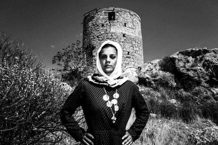 A woman dressed in the traditional costume of Kalymnos, standing before the local castle of Chryssocherias.