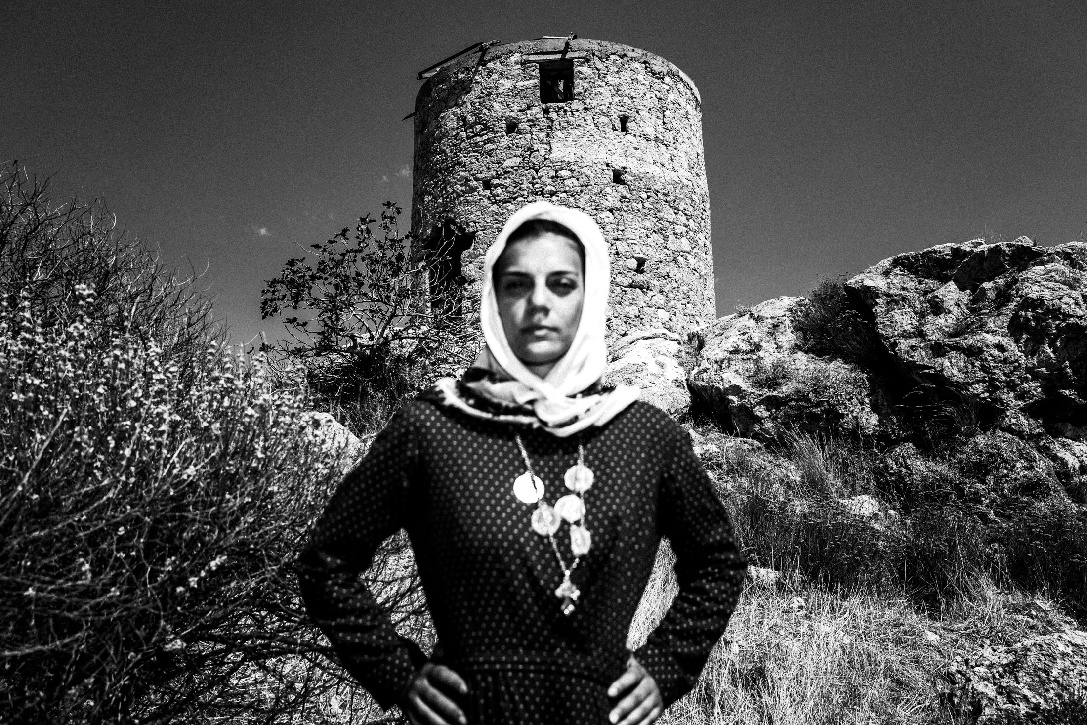 A woman dressed in the traditional costume of Kalymnos, standing before the local castle of Chryssocherias.