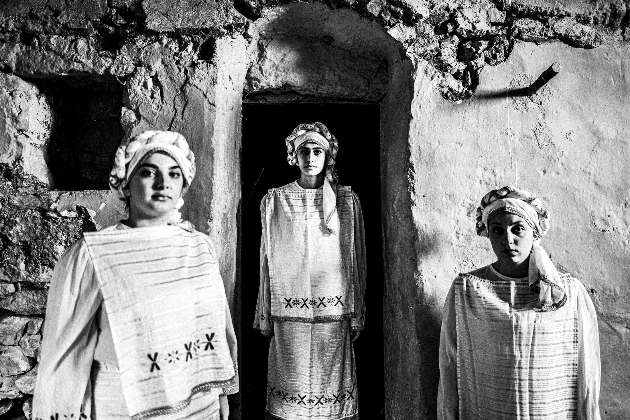 Three women wearing the local costumes of Dafnonas, standing inside a local stone house