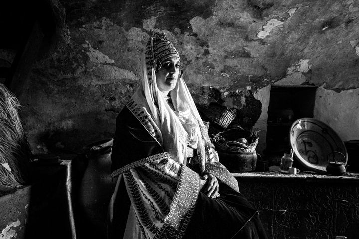 A woman wearing the local bridal costume of Astypalaea, sitting inside a local house